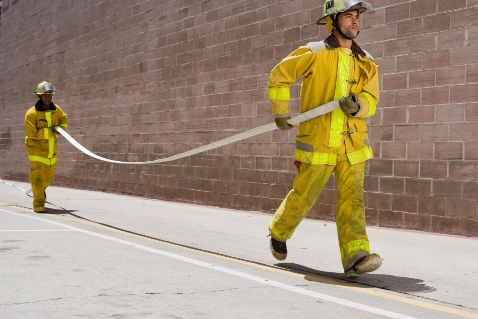 Firefighters in yellow suits carrying hose.