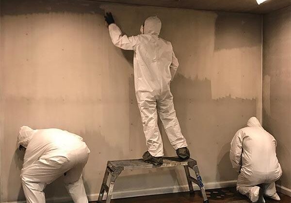 Three workers in protective suits cleaning wall.